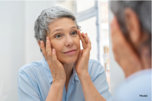 Portrait of mature woman massaging her face while checking wrinkled eyes in the mirror thinking about getting a mini facelift-img-blog