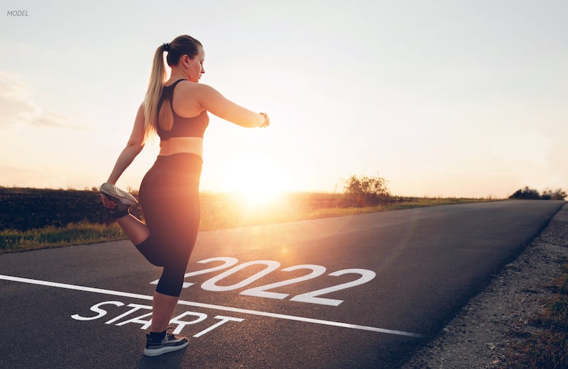 Woman standing at a 2022 starting line, stretching.