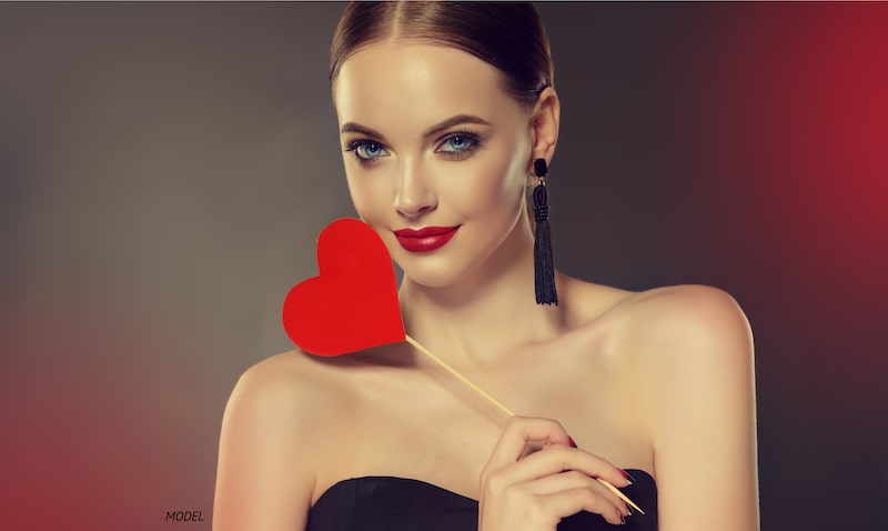 Young, beautiful woman holding a heart cut-out on a stick. Valentine's Day concept.