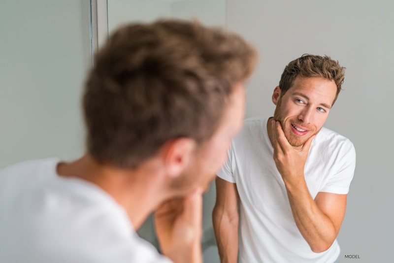  Attractive man in a white shirt looking and smiling at his reflection in the mirror