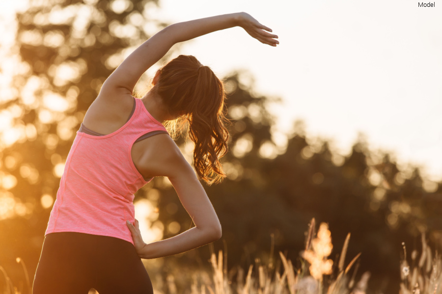 young woman in athletic attire, stretching her arms at a park